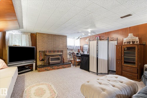 Finished room featuring a brick fireplace with a raised hearth, wood paneling, and wall-to-wall carpeting - 9747 67 Avenue, Edmonton, AB 