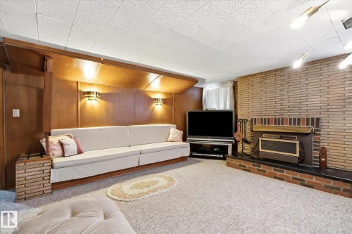 Recreational room with a brick accent wall, built-in fireplace, and wood-paneled feature wall with sconce lighting - 9747 67 Avenue, Edmonton, AB 