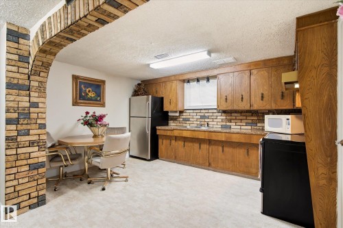 Kitchenette featuring a brick archway, wood cabinetry, light-toned flooring, and a tiled backsplash - 9747 67 Avenue, Edmonton, AB 