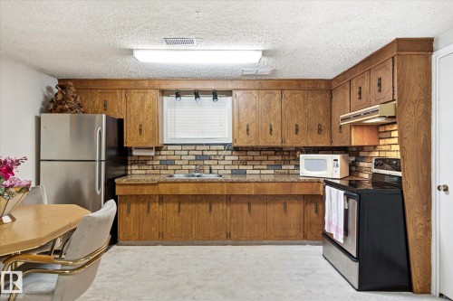 Kitchen featuring wood cabinetry, brick-patterned backsplash, and durable countertop surfaces - 9747 67 Avenue, Edmonton, AB 