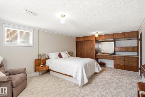 Bedroom featuring extensive built-in wooden cabinetry, a built-in vanity with a mirror, and an integrated headboard with floating bedside tables - 9747 67 Avenue, Edmonton, AB 