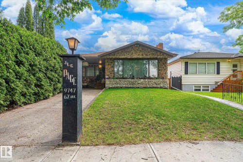 Stone facade residence featuring a prominent front lawn, concrete driveway, and mature landscaping - 9747 67 Avenue, Edmonton, AB 