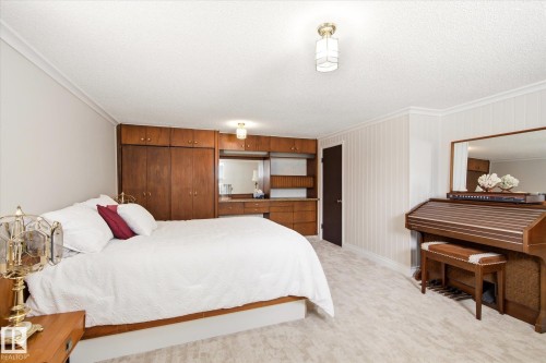 Spacious room featuring light-colored carpet flooring, crown molding, and a built-in wood cabinetry system with integrated desk space and shelving - 9747 67 Avenue, Edmonton, AB 