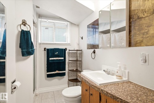 Windowed bathroom featuring a single vanity with a laminate countertop, wood cabinetry, built-in medicine cabinet, and tiled flooring - 9747 67 Avenue, Edmonton, AB 
