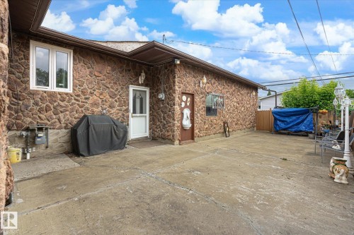 Exterior stone facade featuring a concrete patio, white framed windows, and a white storm door - 9747 67 Avenue, Edmonton, AB 