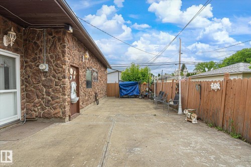 Stone veneer exterior with concrete hardscaping, multiple outdoor light fixtures, and a wooden privacy fence - 9747 67 Avenue, Edmonton, AB 