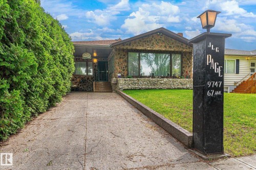 Stone facade home featuring a prominent bay window, concrete driveway, and a manicured lawn - 9747 67 Avenue, Edmonton, AB 