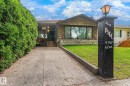 Stone facade home featuring a prominent bay window, concrete driveway, and a manicured lawn - 9747 67 Avenue, Edmonton, AB 
