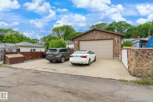 Stone-clad detached garage featuring a light-toned panel door and a concrete driveway offering ample parking - 9747 67 Avenue, Edmonton, AB 