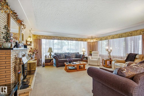 Carpeted living area featuring a prominent brick fireplace with an ornate mantel and hearth - 9747 67 Avenue, Edmonton, AB 