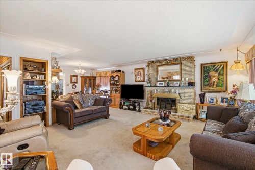 Spacious living area featuring a brick fireplace with a hearth, wall-to-wall carpeting, built-in shelving, and recessed lighting - 9747 67 Avenue, Edmonton, AB 