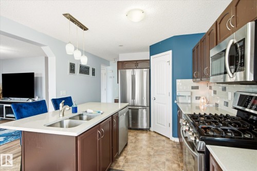 Contemporary kitchen featuring dark wood-finish cabinetry, stainless steel appliances, and a central island with a double sink - 1744 61 Street, Edmonton, AB 