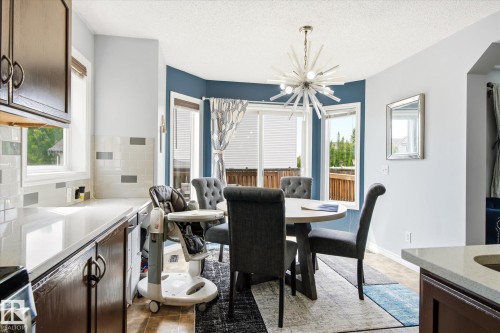 Open concept dining area featuring a contemporary sputnik chandelier, bay windows, and wood-finish flooring - 1744 61 Street, Edmonton, AB 