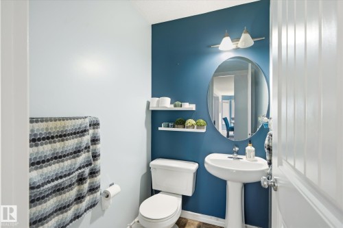 Pedestal sink with chrome faucet, oval mirror, and wall-mounted lighting fixture - 1744 61 Street, Edmonton, AB 