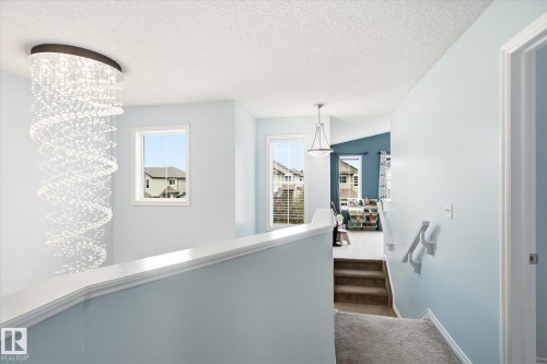Spiral crystal chandelier illuminating a landing with a white railing, soft blue walls, and carpeted stairs - 1744 61 Street, Edmonton, AB 
