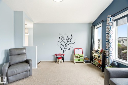 Bright interior space featuring a light-colored carpet, a half-wall partition, and a contrasting accent wall with two large windows - 1744 61 Street, Edmonton, AB 