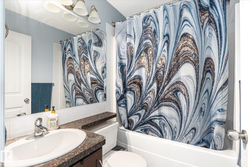 Bathroom featuring a drop-in sink, dark countertop, white subway tile backsplash, and a four-bulb vanity light fixture - 1744 61 Street, Edmonton, AB 