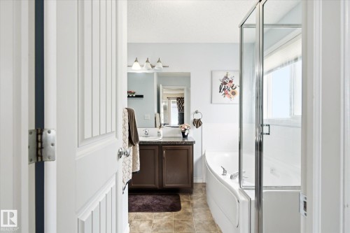 Bathroom featuring a corner soaking tub with glass enclosure, white ceramic tile surround, and a window with privacy blinds - 1744 61 Street, Edmonton, AB 