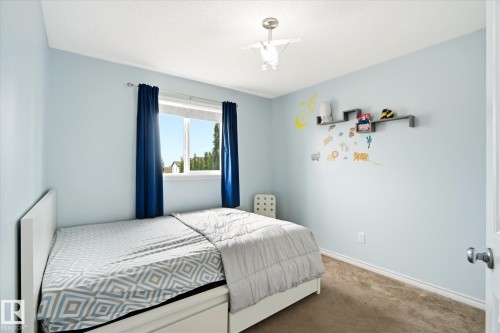 Carpeted room with a ceiling-mounted light fixture, a window with a white frame, and a wall-mounted floating shelf unit - 1744 61 Street, Edmonton, AB 