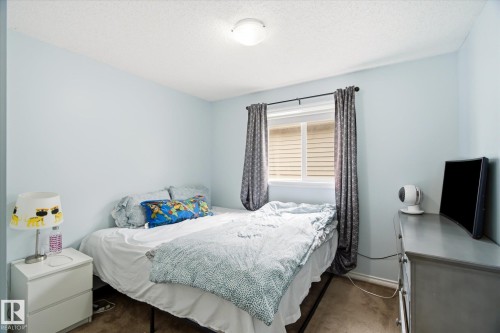 Bedroom featuring a single window with blinds and dark-toned curtains, light blue wall paint, and textured carpet flooring - 1744 61 Street, Edmonton, AB 