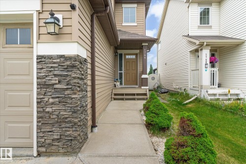 Stone veneer accents complementing beige siding, a concrete pathway, and a brown front door with transom window - 1744 61 Street, Edmonton, AB 