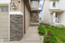 Stone veneer accents complementing beige siding, a concrete pathway, and a brown front door with transom window - 1744 61 Street, Edmonton, AB 