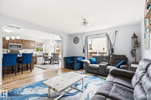 Open-concept living space featuring wood-finish flooring, a kitchen island with seating, pendant lighting, and recessed ceiling lights - 1744 61 Street, Edmonton, AB 