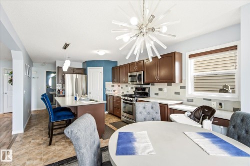 Contemporary kitchen featuring a starburst chandelier, stainless steel appliances, dark wood cabinetry, and a kitchen island with a built-in sink - 1744 61 Street, Edmonton, AB 