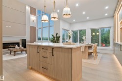 Open-concept living space featuring a central island with a light wood-finish base and light-toned countertop, a multi-pane window wall, recessed ceiling lighting, a contemporary fireplace, and wood-finish flooring - 
