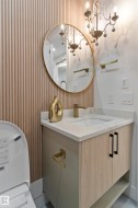 Vanity area featuring a gold-framed circular mirror, a decorative chandelier, and fluted paneling - 