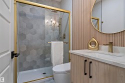 Contemporary bathroom featuring a walk-in shower with gold-framed glass enclosure, hexagonal tile surround, and a vanity with light wood-finish cabinetry, white countertop, and gold-finish faucet - 