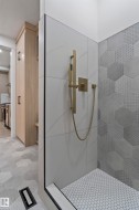 Walk-in shower featuring a brass-finish shower system, large format white tile with subtle veining, and a complementary hexagonal textured tile accent wall - 