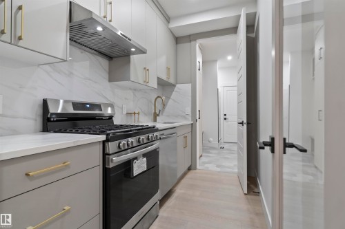 Kitchen featuring a stainless steel range with overhead hood, white countertops, and a full-height marble-patterned backsplash - 3305 Chickadee Drive, Edmonton, AB 