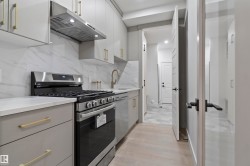Kitchen featuring a stainless steel range with overhead hood, white countertops, and a full-height marble-patterned backsplash - 
