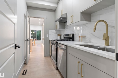 Galley kitchen with light gray cabinetry, stainless steel appliances, a double basin sink, and a gold-finish faucet - 3305 Chickadee Drive, Edmonton, AB 