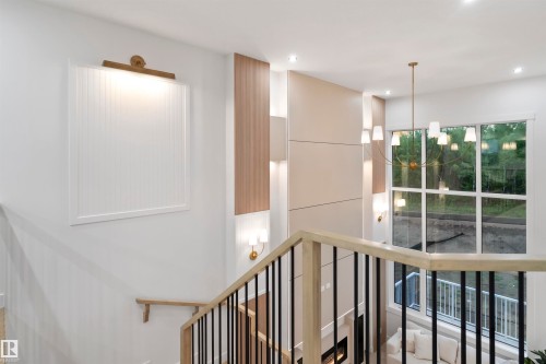 Two-story living area featuring a prominent window wall, a modern chandelier, a fireplace with integrated shelving, and a sleek staircase with light wood banisters and black spindles - 3305 Chickadee Drive, Edmonton, AB 