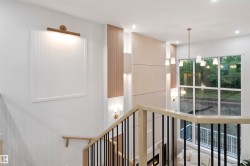 Two-story living area featuring a prominent window wall, a modern chandelier, a fireplace with integrated shelving, and a sleek staircase with light wood banisters and black spindles - 