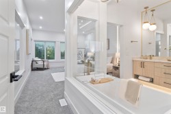Freestanding soaking tub with a glass partition, custom wood-finish vanity with a light-toned countertop, and dual pendant lighting fixtures - 