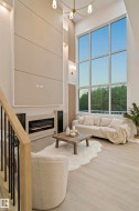 Two-story living area featuring a full-height window wall, light wood-finish flooring, a built-in electric fireplace, recessed lighting, and an overhead chandelier - 