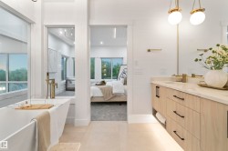 Luxurious bathroom featuring a freestanding soaking tub with a floor-mounted gold-tone faucet, a double vanity with a light wood-finish cabinet, stone countertop, and pendant lighting - 