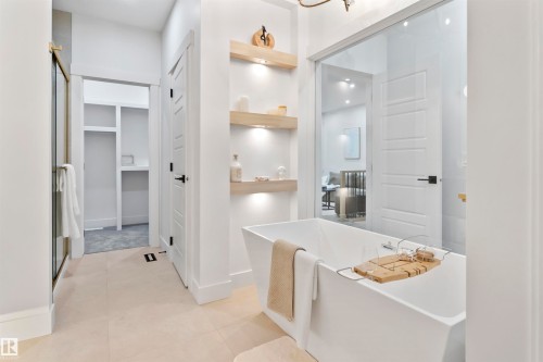 Freestanding soaking tub with a modern square profile, complemented by warm wood-finish floating shelves featuring integrated lighting - 3305 Chickadee Drive, Edmonton, AB 
