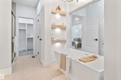 Freestanding soaking tub with a modern square profile, complemented by warm wood-finish floating shelves featuring integrated lighting - 