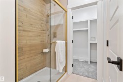 Glass-enclosed shower with gold-tone fixtures, wood-finish tile surround, and built-in shelving - 