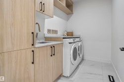 Laundry area featuring light wood-finish cabinetry with black hardware, a utility sink with a brass-finish faucet, and a light-toned countertop - 