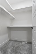 Walk-in closet with layered shelving, integrated hanging rod, plush grey carpeting, white baseboards, and a modern paneled door with matte black hardware - 