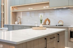 Kitchen island with a light-toned countertop, integrated cooktop, brass-finish faucet, under-cabinet lighting, and built-in oven - 