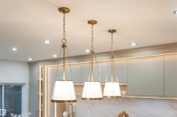 Three brass pendant lights with pleated shades illuminate a modern kitchen space - 
