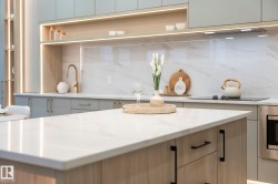 Kitchen island featuring a white stone countertop, light wood-finish cabinetry, and matte black hardware - 