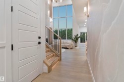Entryway featuring light wood-finish flooring, a contemporary staircase with integrated lighting, a sleek black metal railing, and a large multi-pane window wall - 