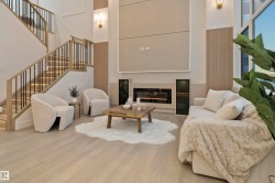 Double-height living area featuring a modern fireplace with built-in cabinetry, light wood-finish flooring, and a contemporary staircase with black metal balusters - 